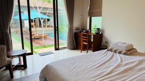 Habitación de hotel con cama, escritorio y vista al área de piscina exterior.