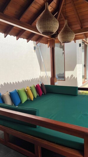 A covered outdoor seating area with a green cushioned bench and colorful cushions, under a wooden roof with woven light fixtures. - Eden Collection – 4 Bedroom Luxury Private Pool Villa in Thalpe (Talpe)