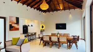 A modern living room with a dining area, a kitchen, and a TV mounted on the wall. - Eden Collection – 4 Bedroom Luxury Private Pool Villa in Thalpe (Talpe)