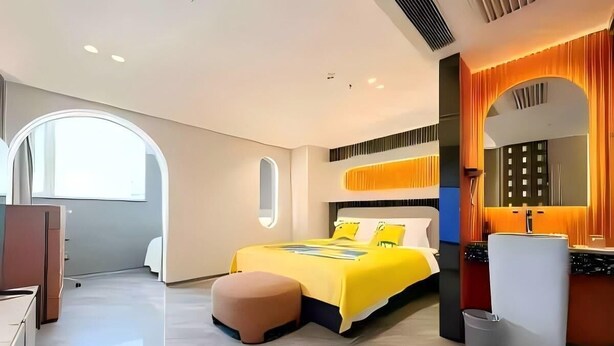 Quarto de hotel moderno com uma cama, um pequeno espaço de estar, uma toucador com espelho e uma janela.