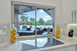 A kitchen with a glass window, a countertop, and a view of a pool and palm trees. - Luxury Coral Springs Retreat (Coral Springs)