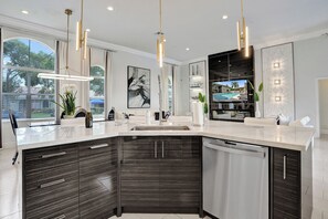 A modern kitchen with a large island, dark cabinetry, and pendant lighting. - Luxury Coral Springs Retreat (Coral Springs)