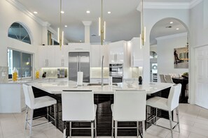 A modern kitchen with white cabinetry, stainless steel appliances, and a central island with seating. - Luxury Coral Springs Retreat (Coral Springs)