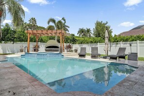 Una piscina con un gazebo, sedie a sdraio e una zona relax ombreggiata.