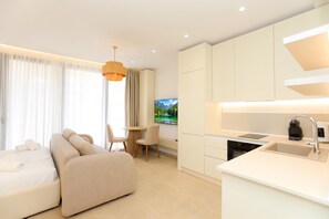 A modern hotel room with a sofa, dining table, chairs, a kitchen area with a sink and stove, and a large window with curtains. - Palm Coastal White Studio, Vlore, Albania (Vlore)