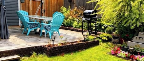 A backyard with a wooden deck, a barbecue grill, and a table with chairs.