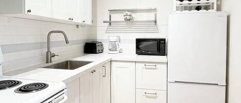 Une cuisine moderne avec des meubles blancs, une cuisinière, un four à micro-ondes et un réfrigérateur à vin.