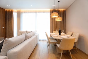Ein modernes Wohnzimmer mit einer Couch, einem Esstisch, Stühlen und einem großen Fenster mit Vorhängen.