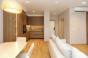 Eine moderne Küche mit Holzschränken, eine Essecke mit weißem Tisch und Stühlen sowie ein Wohnbereich mit einem weißen Sofa.