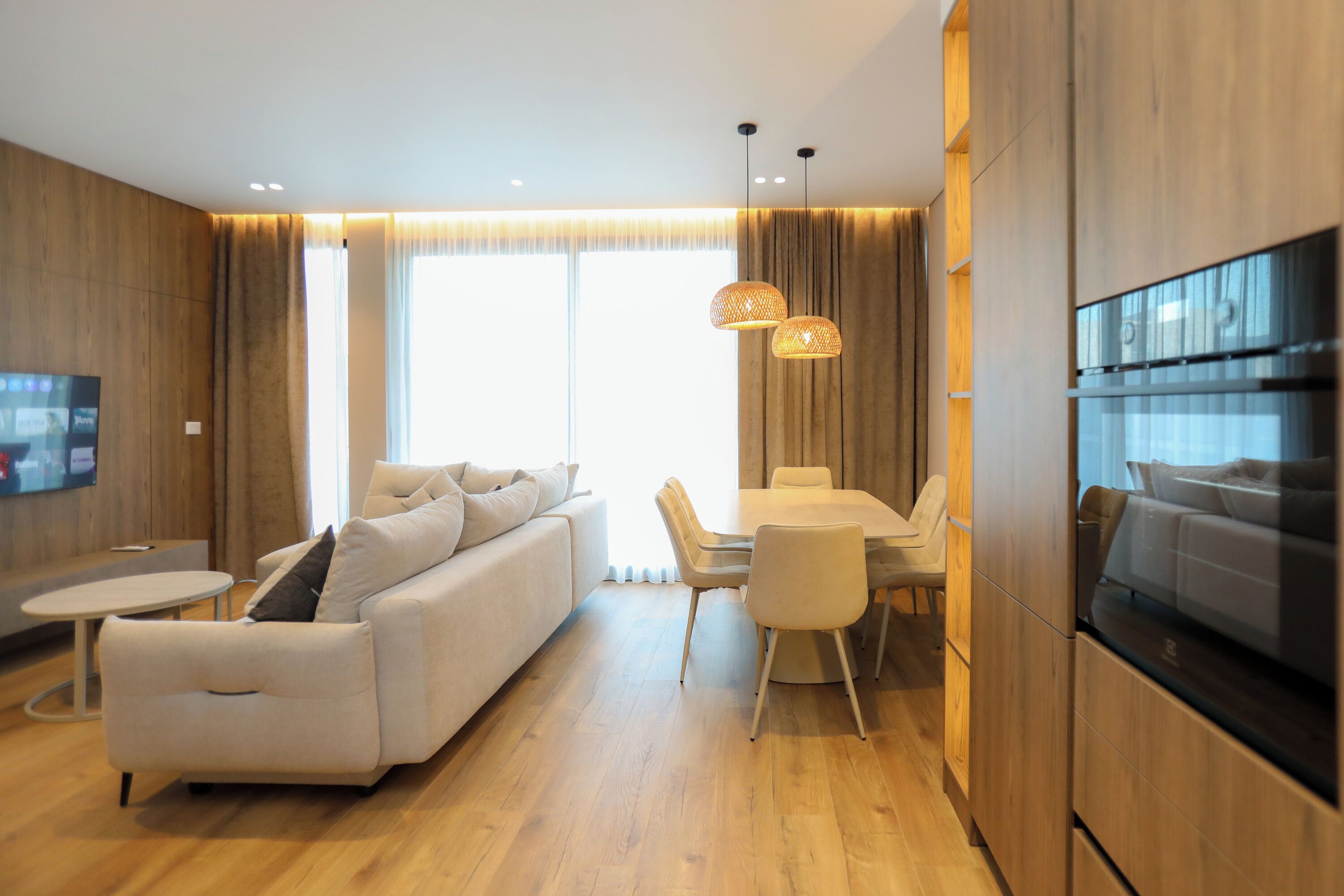 A modern living room with a sofa, dining table, chairs, and a TV mounted on the wall.