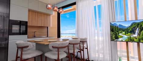 A modern kitchen with a central island, bar stools, and a large window with a scenic view.
