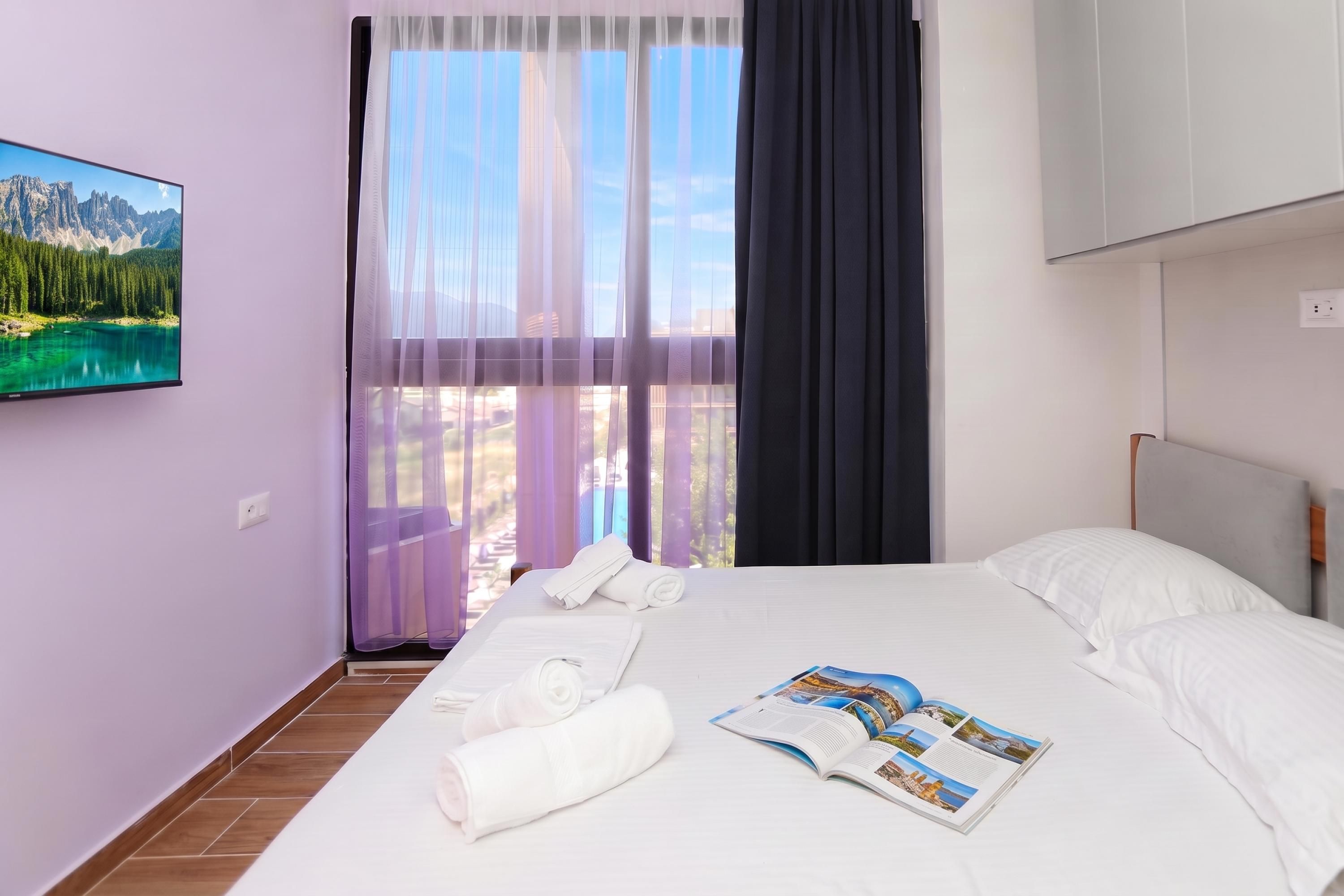 A hotel room with a bed, a window with curtains, a view of mountains, and a magazine on the bed.