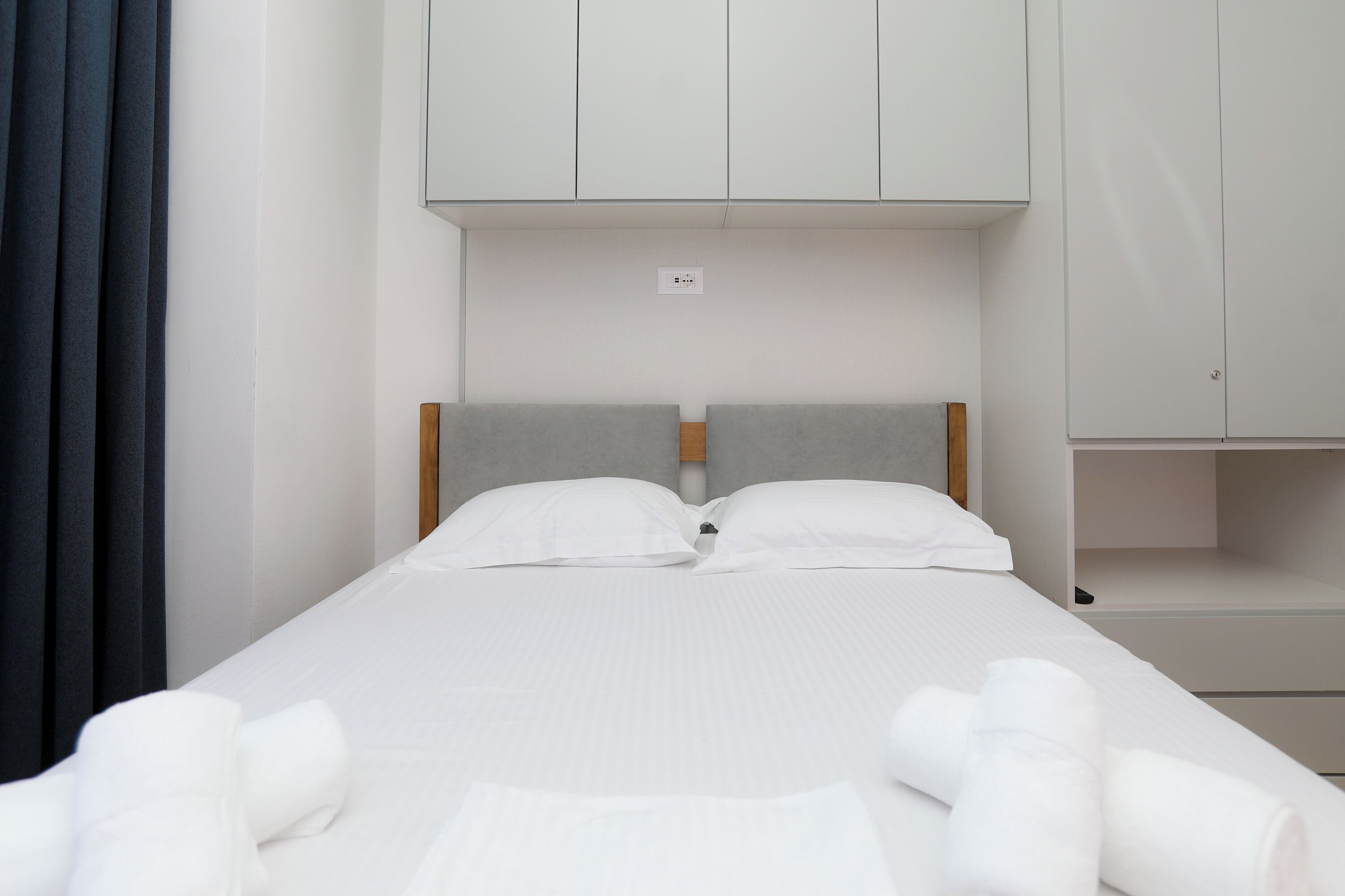 A single bed with white linens and two pillows, a wooden headboard, and a grey headboard.