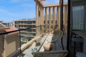 Ein Balkon mit Korbmöbeln, Blick auf andere Gebäude und einen klaren Himmel.