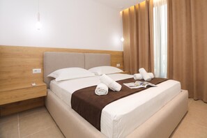 Ein Hotelzimmer mit Bett, Nachttisch, Lampe und einem Fenster mit Vorhängen.