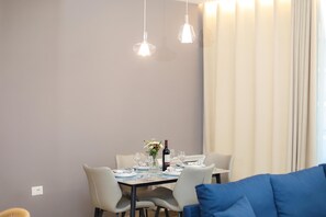 Uma sala de jantar com uma mesa posta para dois, um vaso com flores e uma garrafa de vinho.