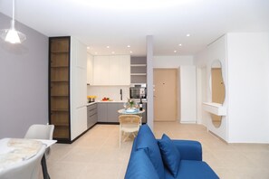A modern living room with a blue sofa, a dining table with chairs, and a kitchen area with cabinets and a countertop. - Sea Side Palm Modern Suites, Vlore, Albania (Vlore)