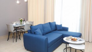 Un salon moderne avec un canapé bleu, une table à manger avec des chaises et une petite table ronde sur laquelle se trouvent une tasse et un muffin.