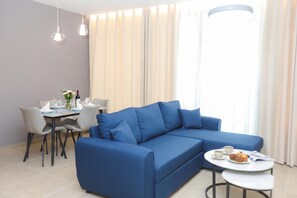 Ein modernes Wohnzimmer mit einem blauen Sofa, einem Esstisch mit Stühlen und einem kleinen runden Tisch mit Tasse und Muffin.