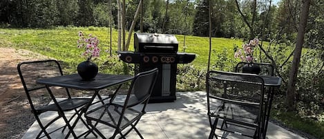 Un patio exterior con una parrilla, dos sillas y una mesa.