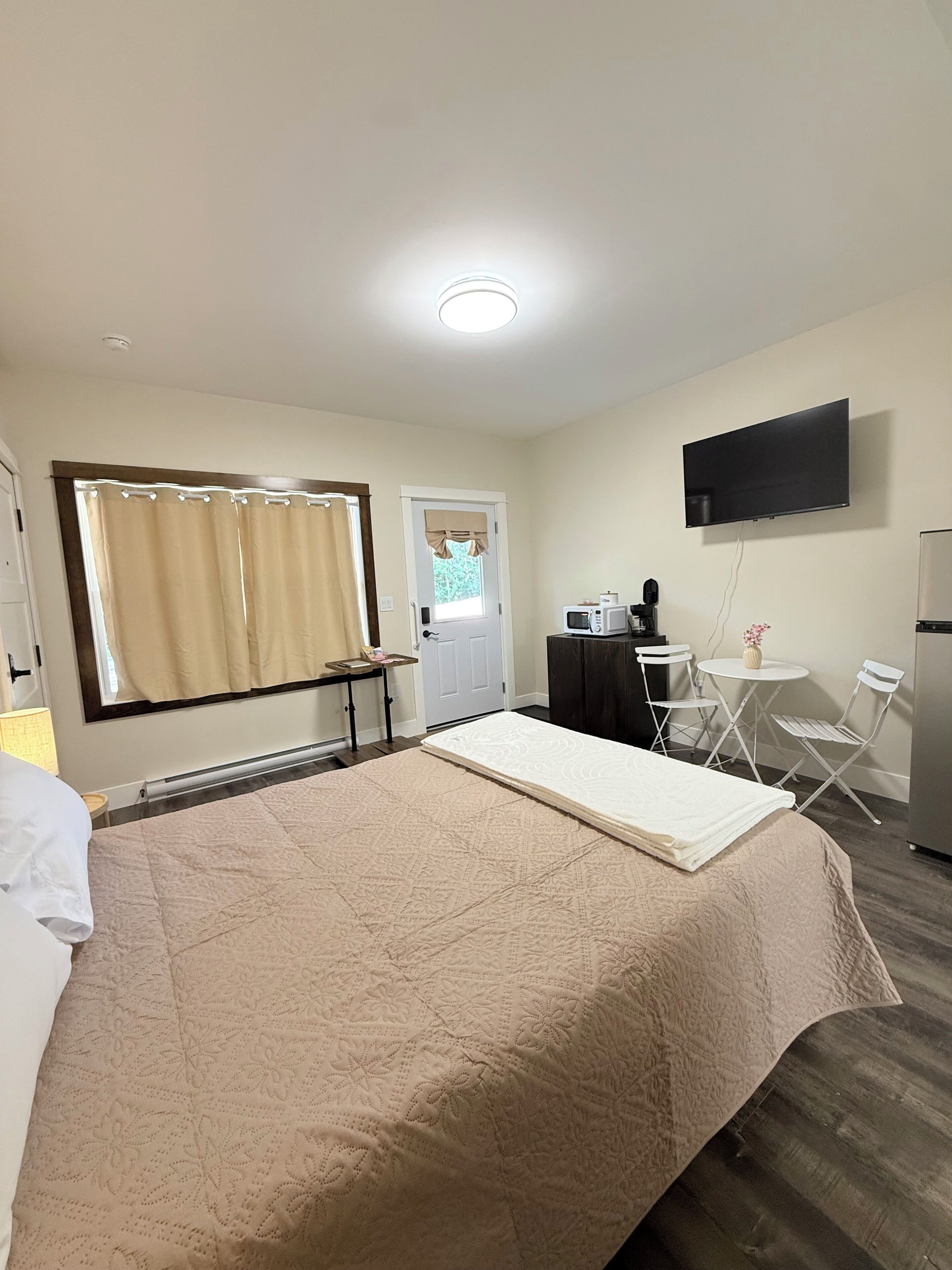 A hotel room with a bed, a desk with a chair, a television, and a window with curtains.