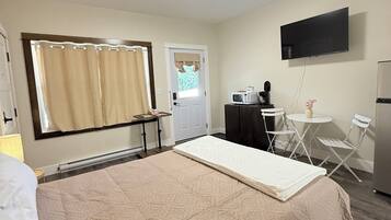 A hotel room with a bed, a desk with a chair, a television, and a window with curtains.