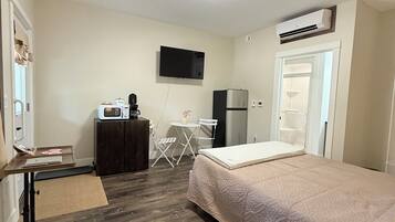 A bedroom with a bed, a desk, a chair, a TV, and an air conditioning unit.