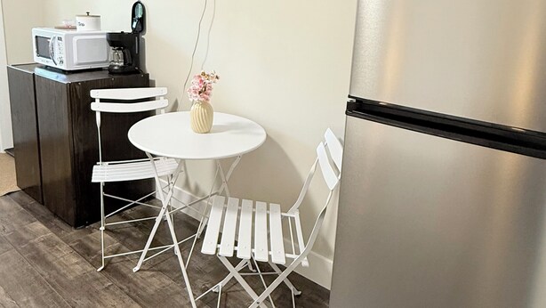 Een ruimtelijk keukenhoekje met een magnetron, koffiezetapparaat en een eettafeltje met stoelen. Een flatscreen televisie is aan de muur boven het tafeltje bevestigd.