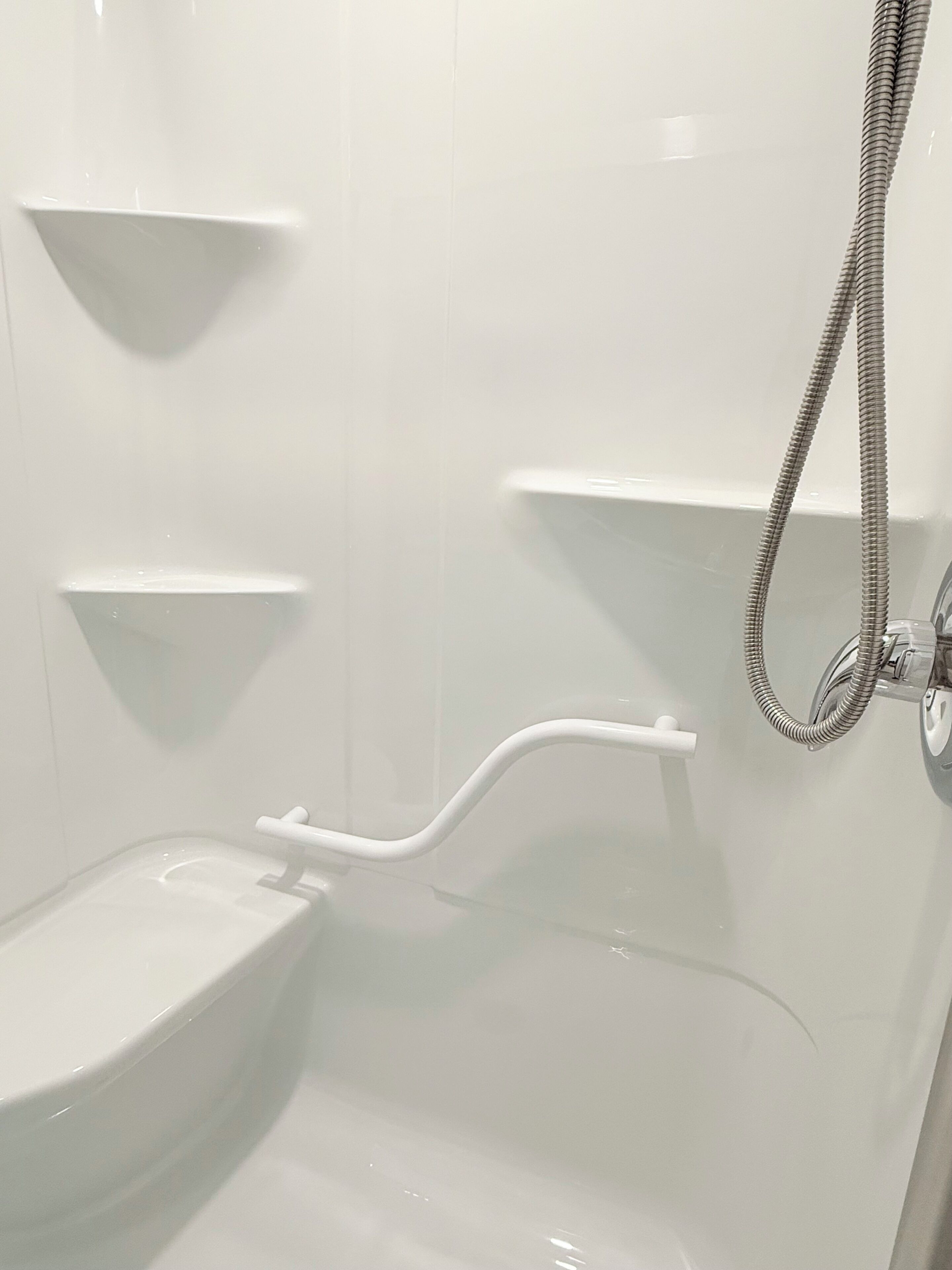 A bathroom with a white toilet, a shower with a hose, and two white shelves.