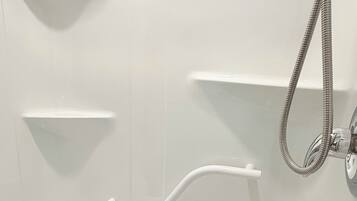 A bathroom with a white toilet, a shower with a hose, and two white shelves.