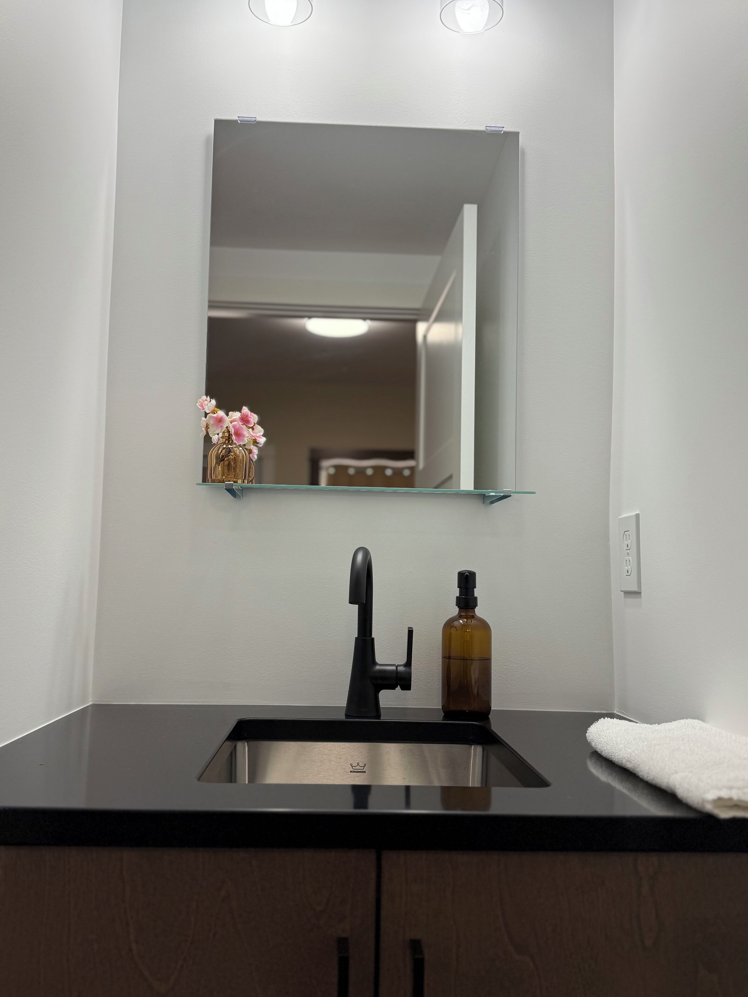 A bathroom with a black sink, a mirror, a bottle of soap, and a towel.