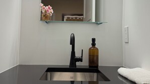 Een badkamer met een zwarte wastafel, een spiegel, een zeepfles en een handdoek.