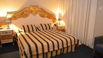 Een hotelkamer met een groot bed, twee nachtkastjes met lampen, een blauwe fauteuil en een decoratief hoofdeinde.