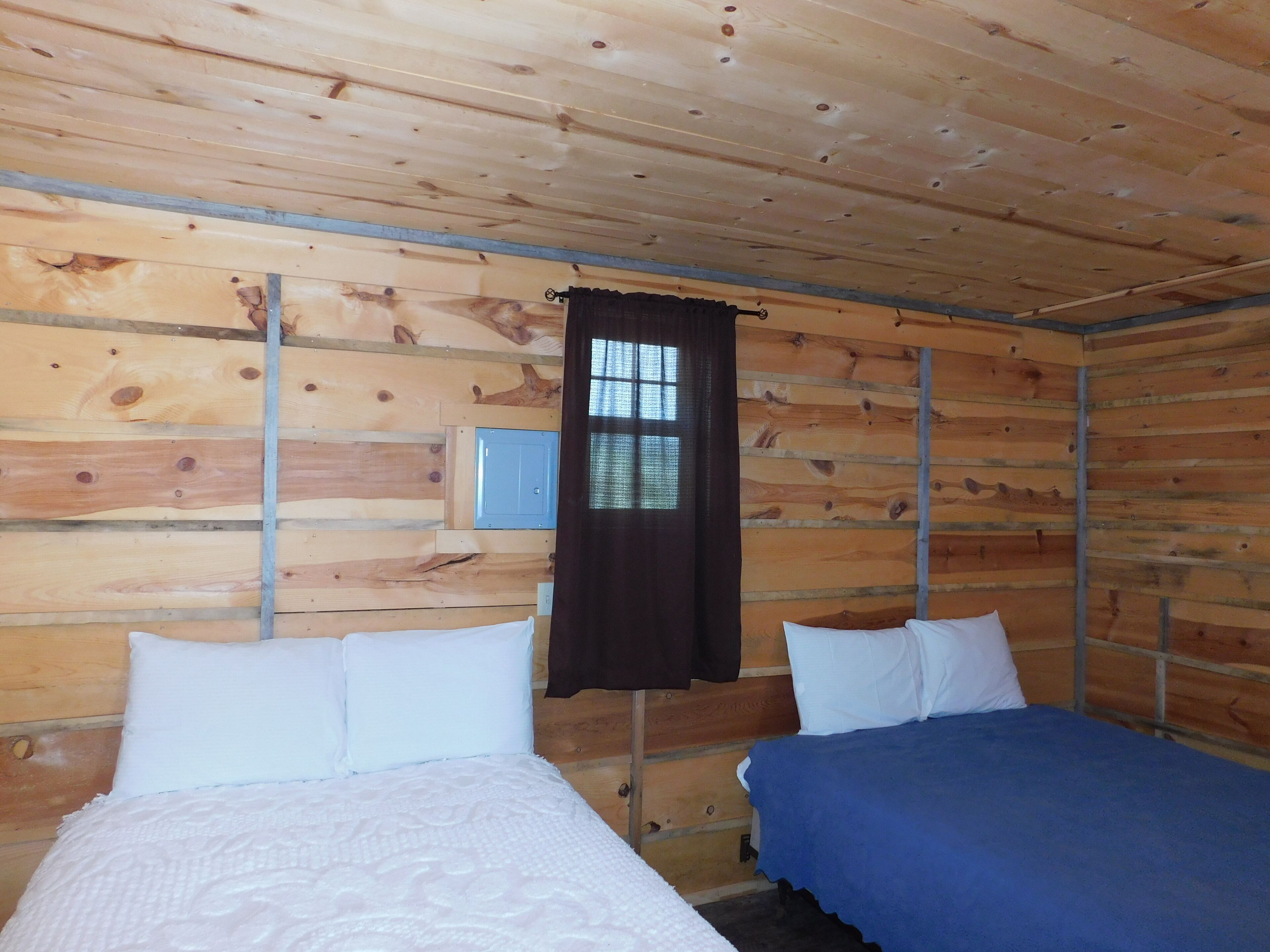 A cabin with two beds, wooden walls, a window with curtains, and a small television.