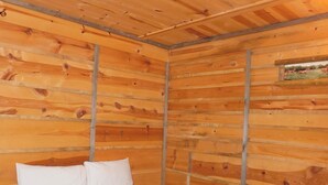 A wooden cabin room with a bed, pillows, and a small painting on the wall. - May's Corner Cabin (Sturgis)