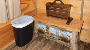A wooden cabin interior with a bench, a trash bin, and a rustic wall. - May's Corner Cabin (Sturgis)