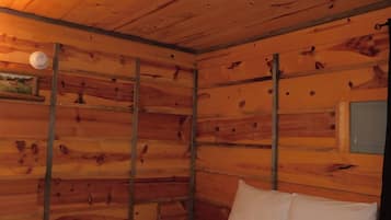 A wooden cabin room with a bed, a wall-mounted light, and a picture.