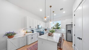 A modern kitchen with white cabinetry, a central island, stainless steel appliances, pendant lighting, and a view to the outdoors. - Modern, luxe HTX Retreat| 8 Min to Toyota/Med Ctr (Houston)