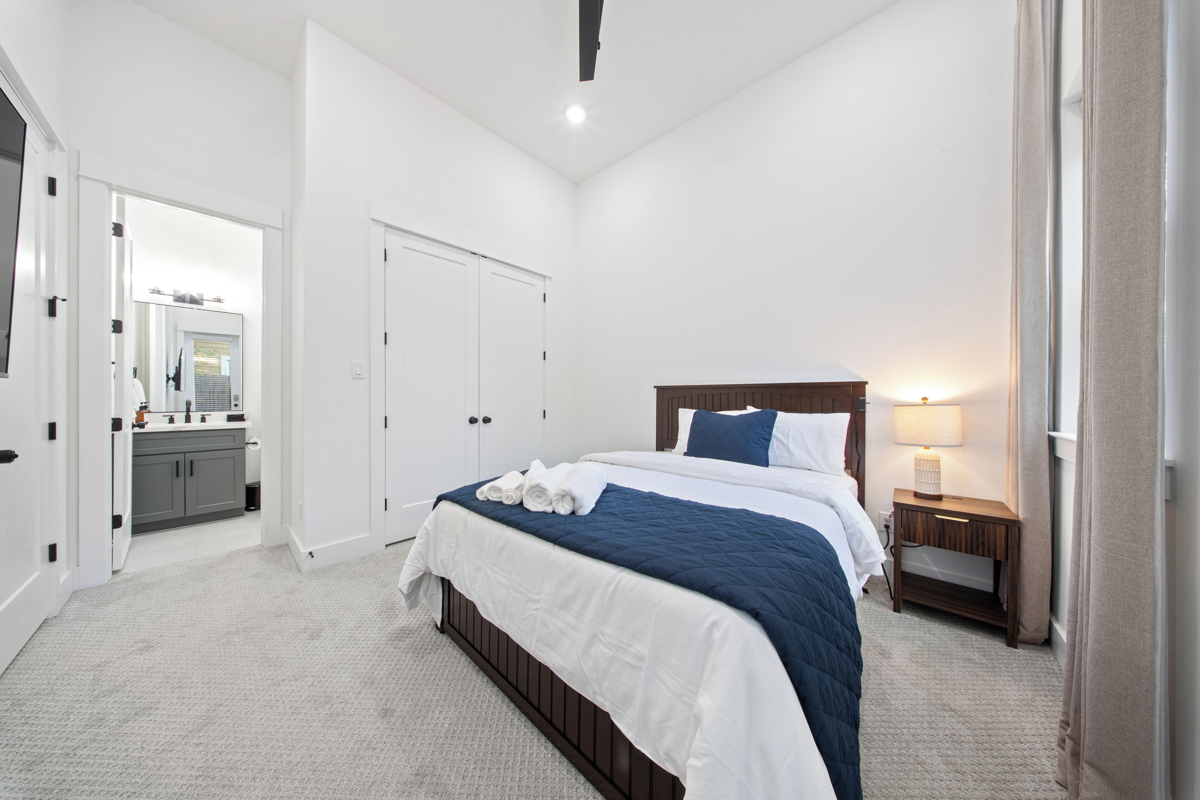 Un dormitorio con cama, mesita de noche, espejo, puerta y baño visible a través de una puerta abierta.