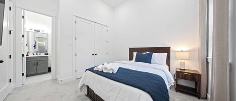 A bedroom with a bed, a nightstand, a mirror, a door, and a bathroom visible through an open door.