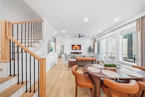 Ein modernes Interieur mit einer Holztreppe, einem Essbereich mit rundem Tisch und Ledersesseln sowie einem großen Fenster mit Jalousien.