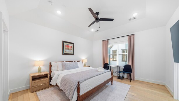 A bedroom with a bed, bedside tables, a desk, a chair, a ceiling fan, and a window with curtains. - Modern, luxe HTX Retreat| 8 Min to Toyota/Med Ctr (Houston)