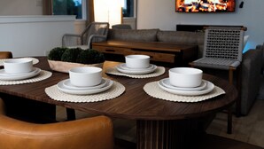 A dining table set with white plates and bowls, a wooden coffee table, a sofa, a chair, and a television displaying a fire. - Modern, luxe HTX Retreat| 8 Min to Toyota/Med Ctr (Houston)