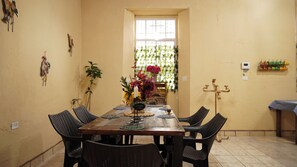 A dining area with a wooden table, wicker chairs, a vase of flowers, and a window with a view of greenery.