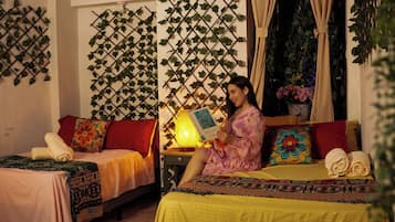 Een kamer met twee bedden, een plant aan de muur, een lamp en een persoon die een boek leest.