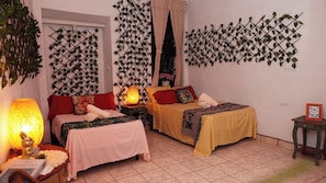 A hotel room with two beds, a nightstand with a lamp, a small table with a picture frame, and decorative vines on the walls.