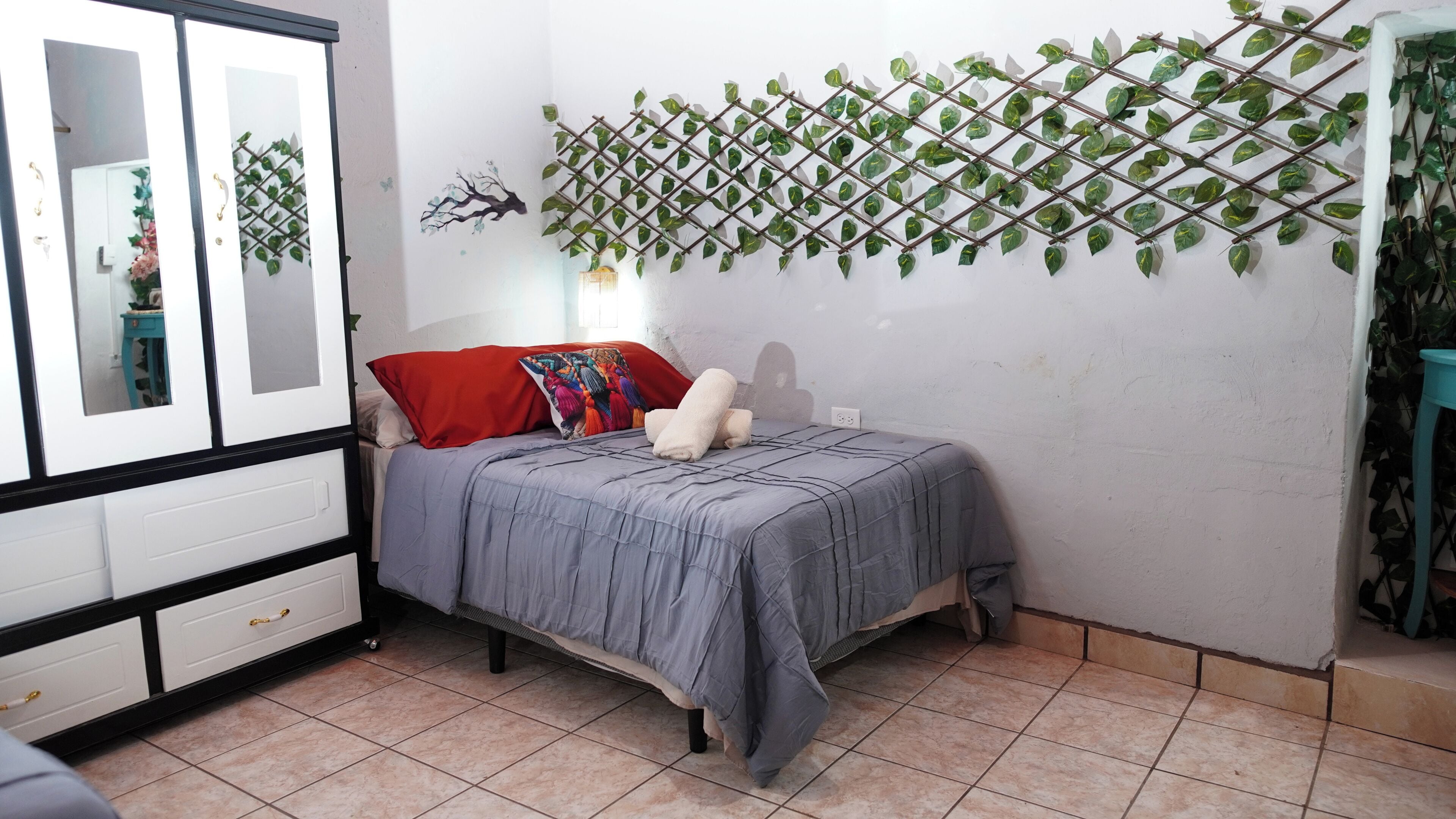 A bedroom with a bed, a wardrobe, a mirror, and a wall-mounted plant.