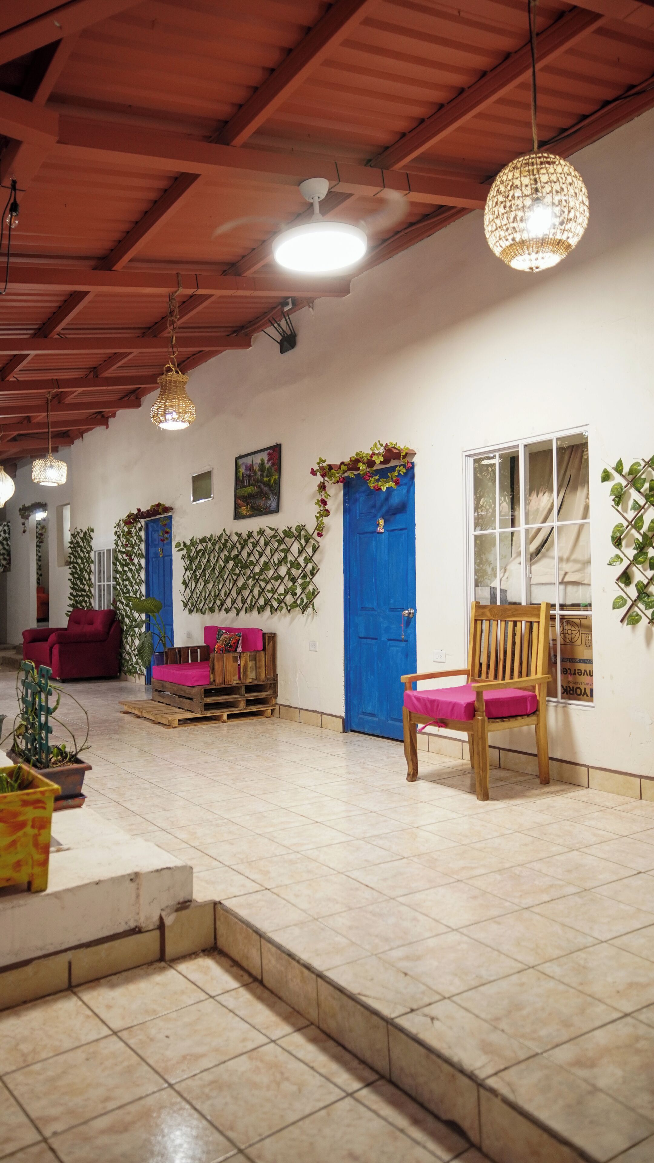 Una habitación amplia con techo alto, una puerta azul, una silla de madera, un sofá rojo y suelo de baldosas.