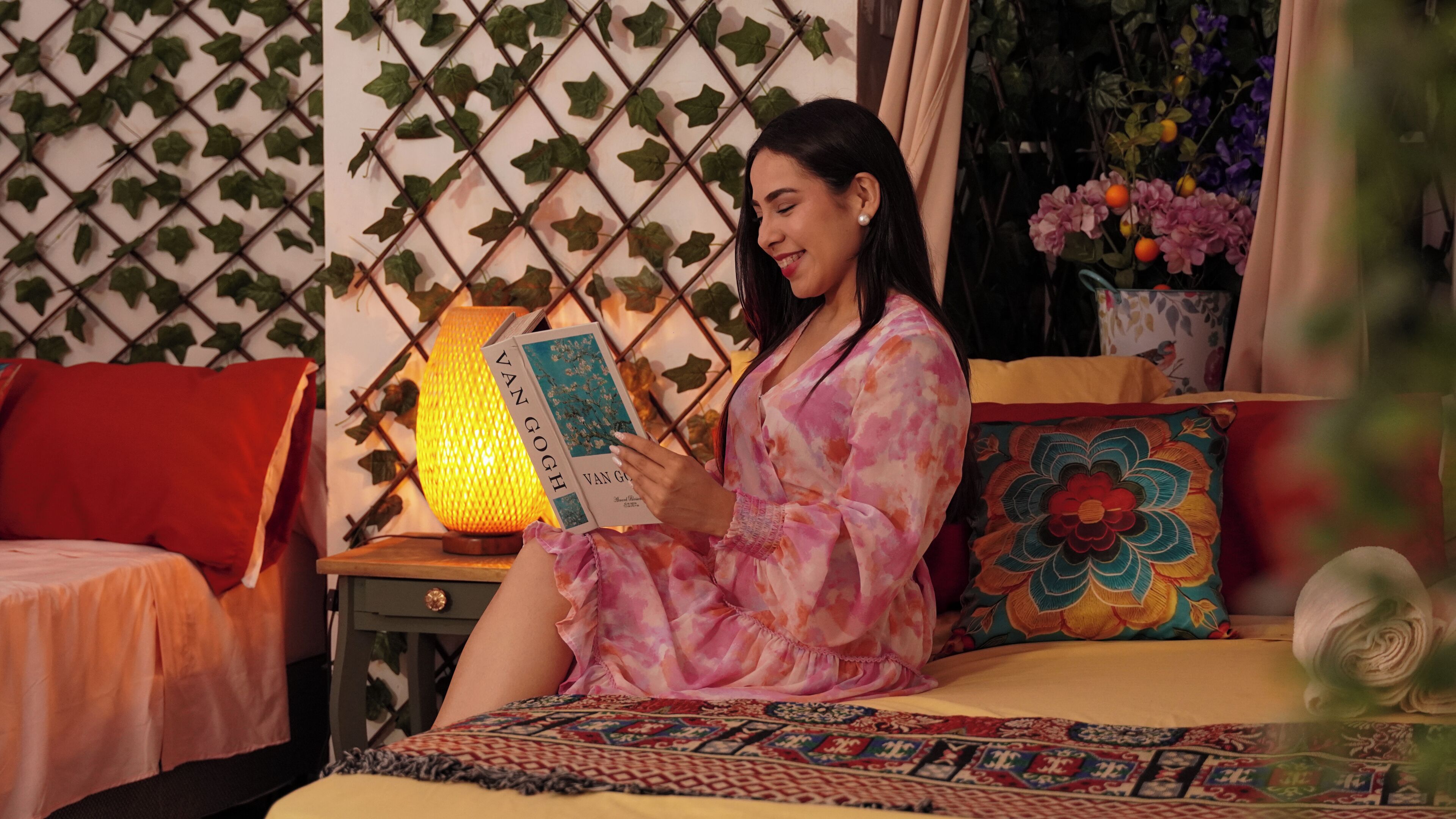 A person sitting on a bed with a book, a lamp, and a wall with a lattice design.