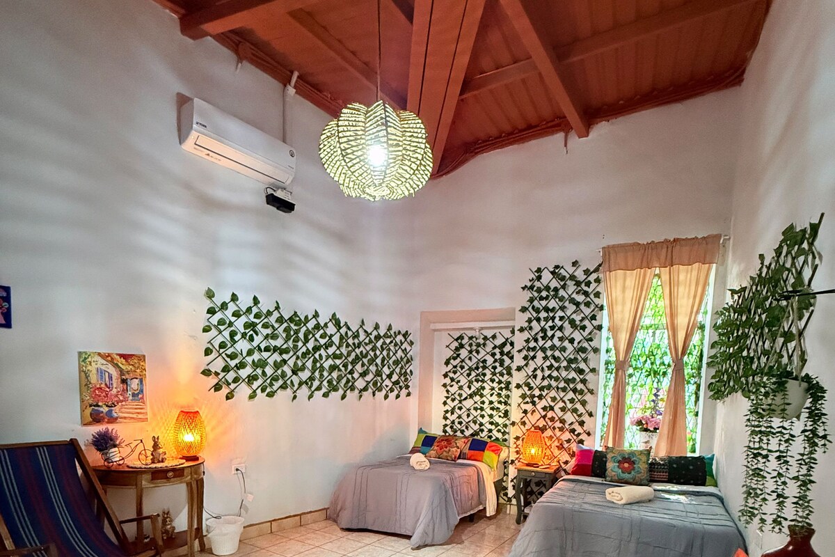A cozy room with a bed, a chair, a table, and a hanging plant wall.